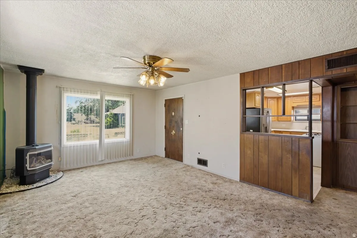 Living area featuring a freestanding fireplace, ceiling fan, and large windows with vertical blinds