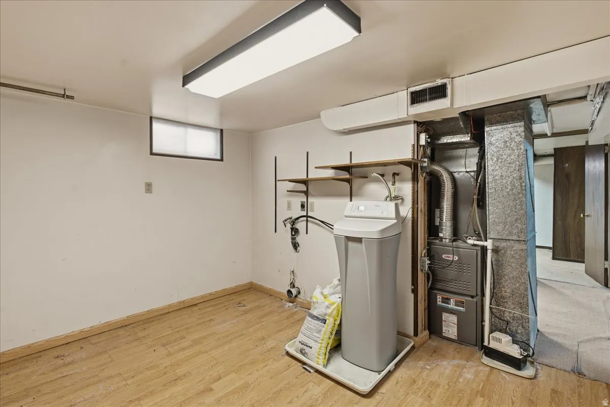 Utility space featuring wood-finish flooring, a functional window, built-in shelving, a water softener, and a furnace