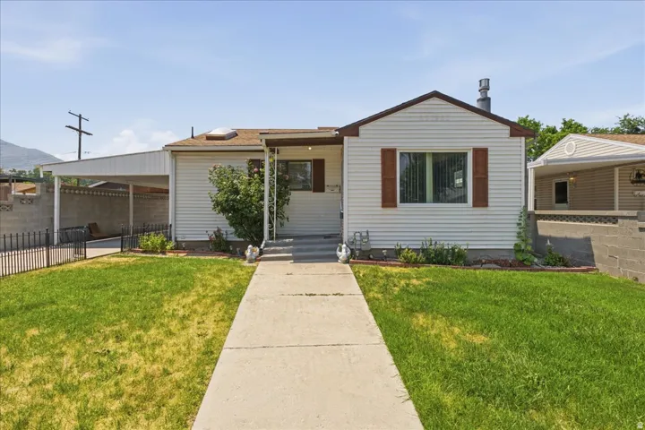 Single-story home featuring a carport, front lawn, concrete pathway, and decorative front shutters