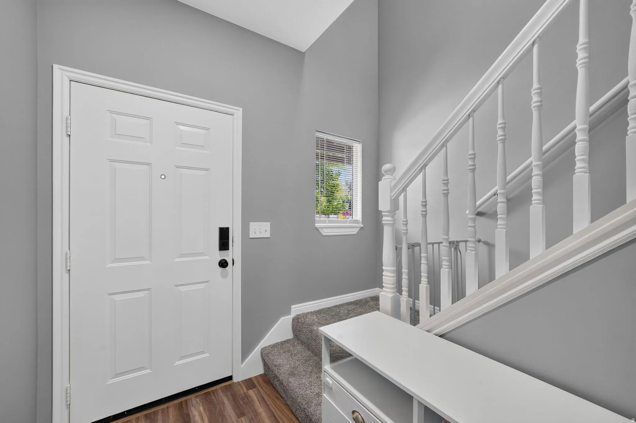 Entryway featuring wood-finish flooring, a six-panel door, and a staircase with white balusters