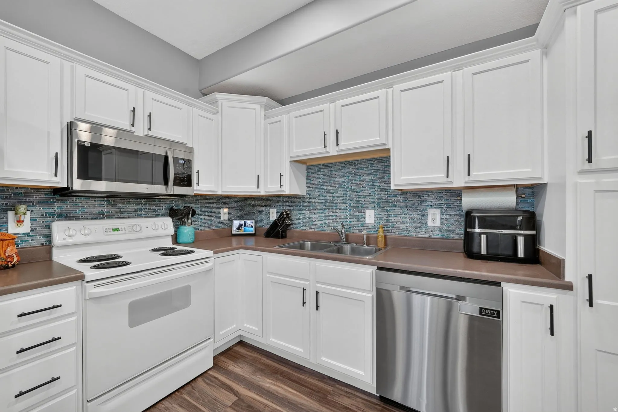 White cabinetry with black hardware, stainless steel microwave, white electric range, stainless steel dishwasher, and wood-finish flooring