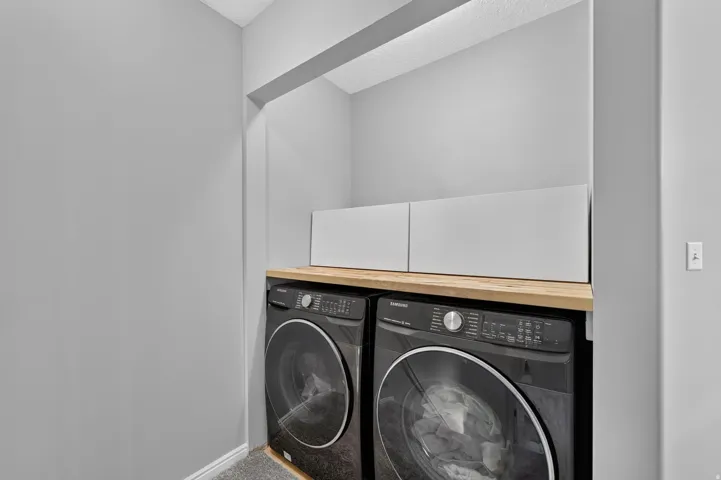 Dedicated laundry area featuring a wood-finish countertop, white cabinetry, and gray walls