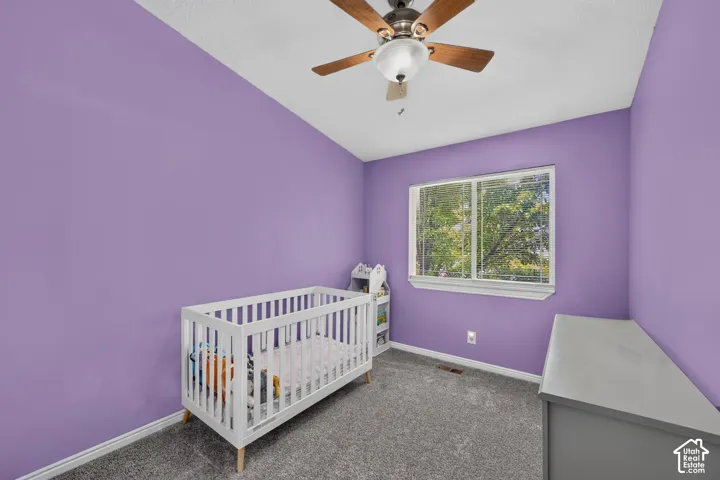 Carpeted room featuring a ceiling fan, a window with exterior tree scenery, baseboards, and painted walls