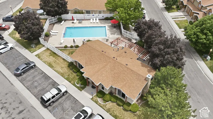Community pool area featuring a blue rectangular swimming pool, white perimeter fencing, lounge chairs, and an adjacent building with a pergola