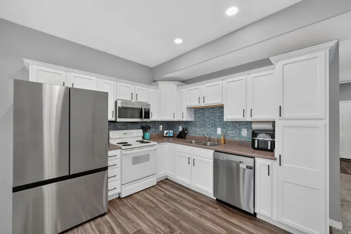 Contemporary kitchen featuring white cabinetry, stainless steel appliances, a blue mosaic tile backsplash, wood-finish flooring, and recessed lighting