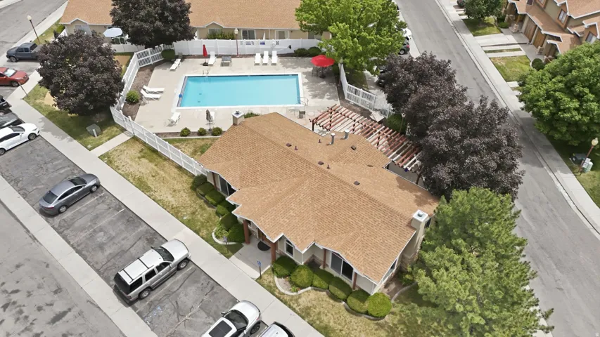 Community pool area featuring a blue rectangular swimming pool, white perimeter fencing, lounge chairs, and an adjacent building with a pergola
