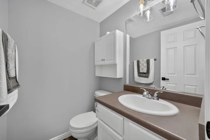Bathroom featuring a white vanity with a brown countertop and integrated sink, chrome faucet, wall-mounted mirror, and overhead lighting