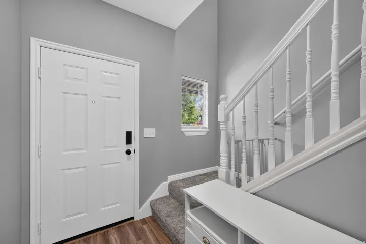 Entryway featuring wood-finish flooring, a six-panel door, and a staircase with white balusters