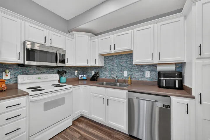 White cabinetry with black hardware, stainless steel microwave, white electric range, stainless steel dishwasher, and wood-finish flooring