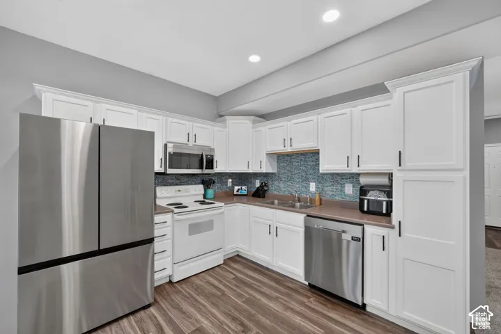 Contemporary kitchen featuring white cabinetry, stainless steel appliances, a blue mosaic tile backsplash, wood-finish flooring, and recessed lighting