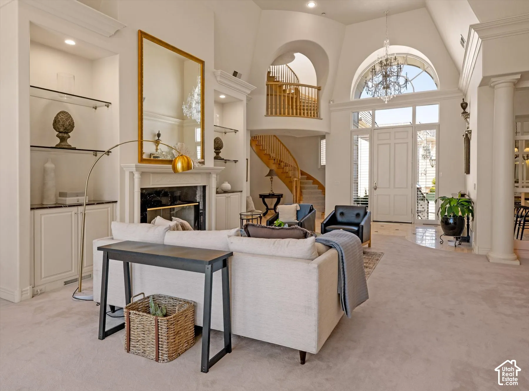Spacious living area featuring a fireplace with a white mantel, built-in shelving with glass inserts, and high ceilings