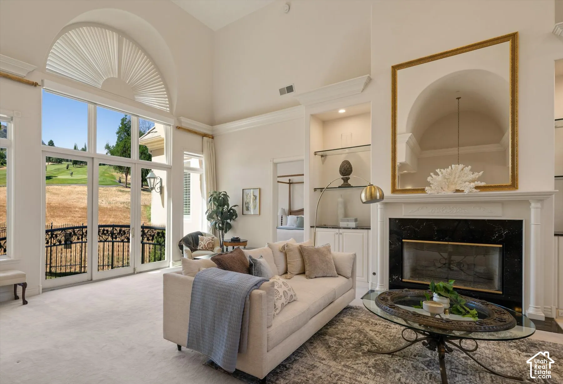 Living space featuring a tall ceiling, a large arched window, and French doors opening to a balcony with an ornate iron railing