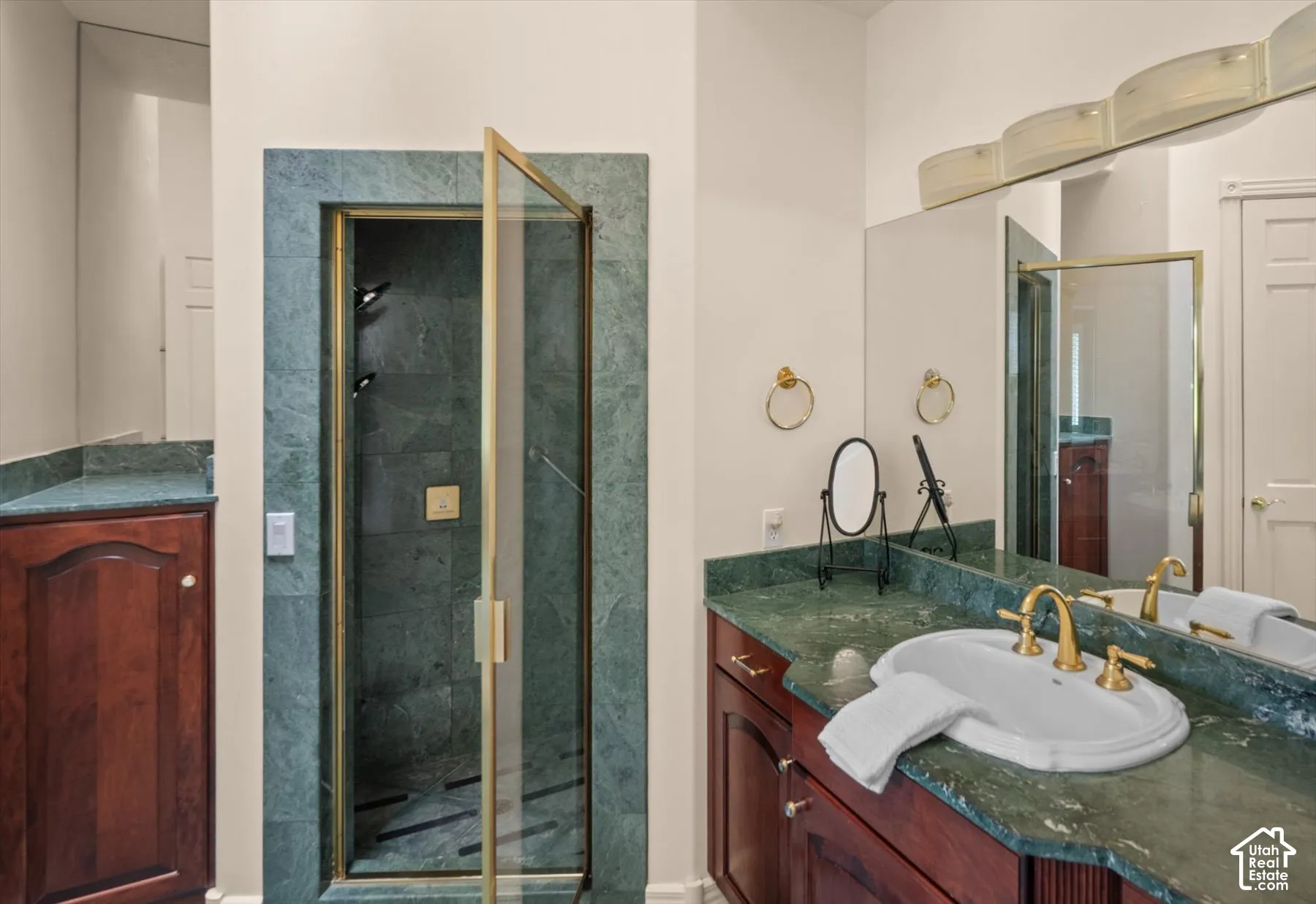 Bathroom featuring a glass-enclosed shower with gold-tone fixtures, a vanity with a green stone countertop, and wood cabinetry