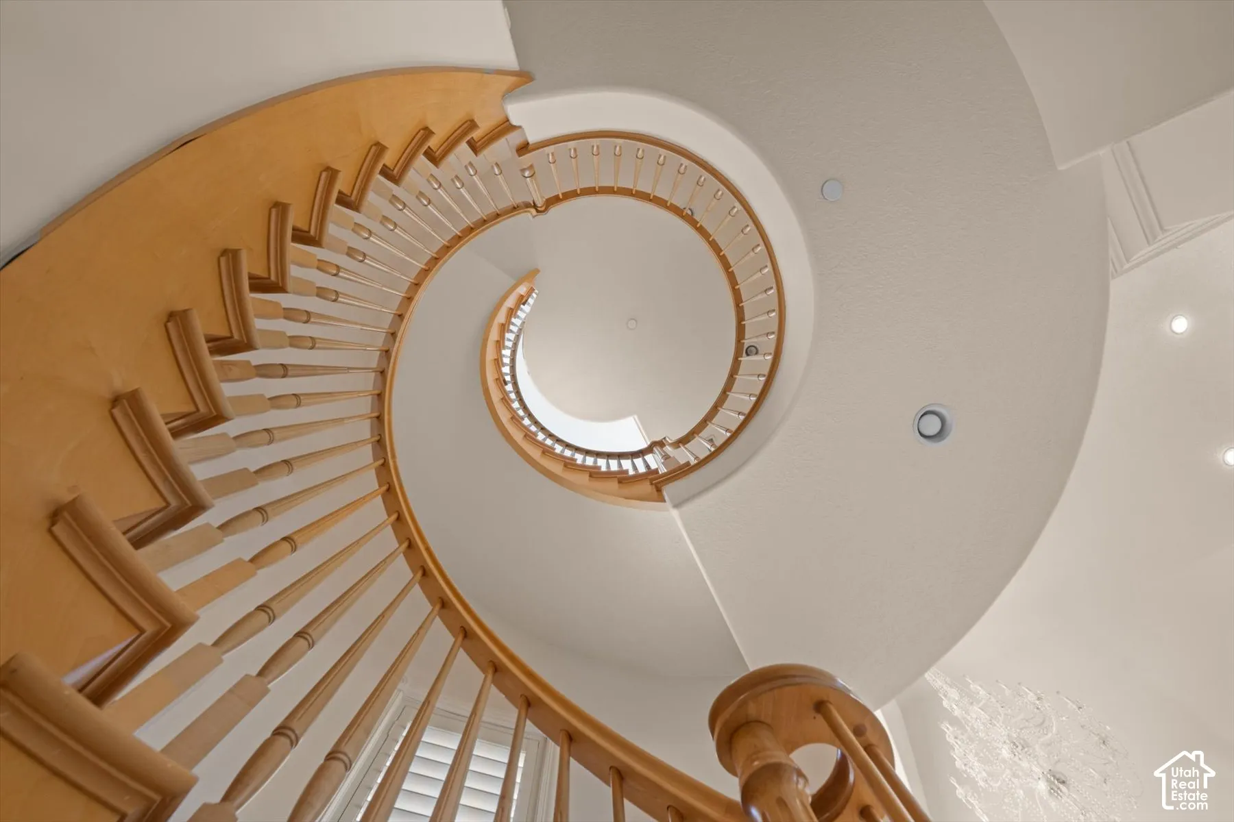 Curving natural wood staircase with balusters, recessed lighting, and white walls