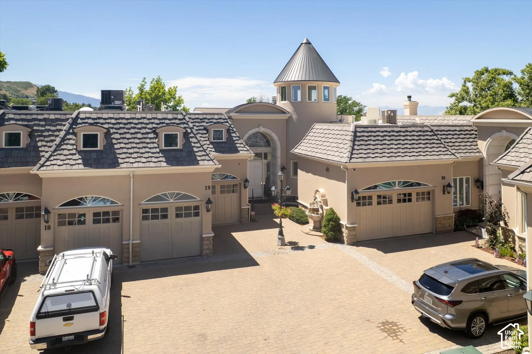 Stucco exterior featuring multiple garage doors with arched transom windows, a distinctive turret, and a paver driveway