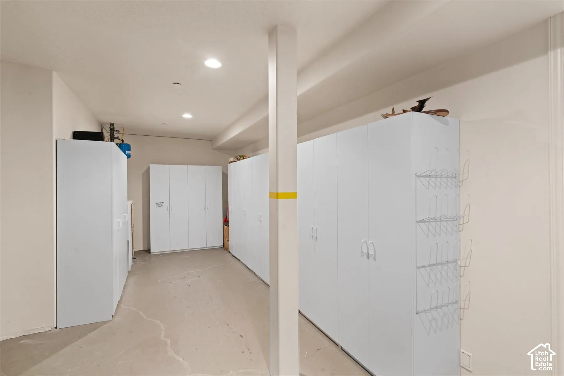 Dedicated storage area featuring multiple white cabinetry units, recessed ceiling lighting, a structural support column, light-toned walls, and concrete flooring