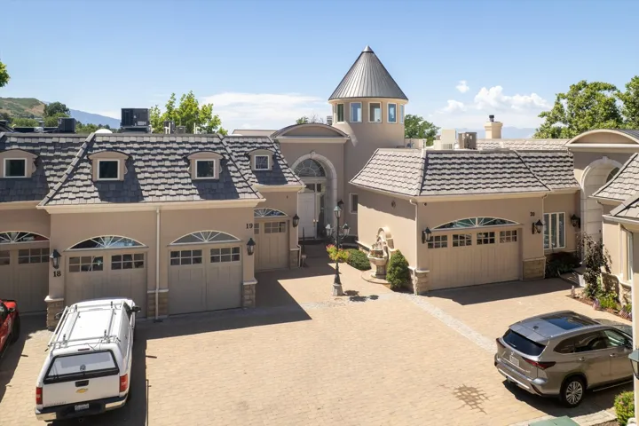 Stucco exterior featuring multiple garage doors with arched transom windows, a distinctive turret, and a paver driveway