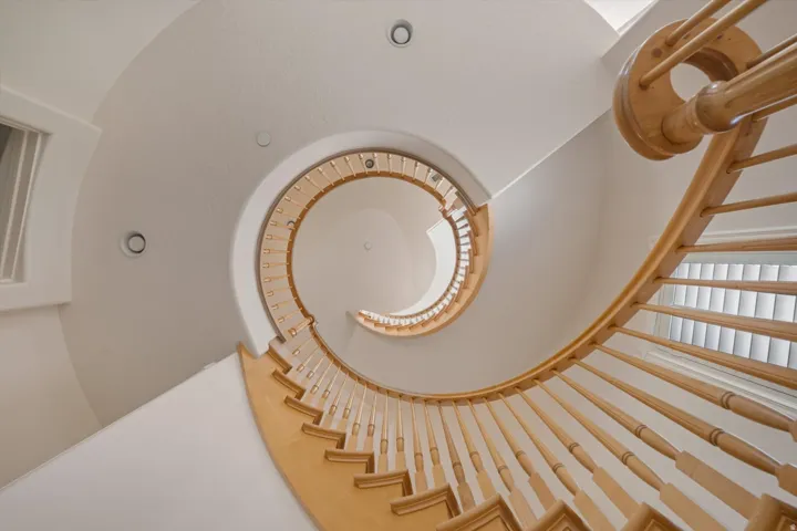 Curved staircase featuring natural wood balusters and handrail, recessed lighting, and  natural illumination