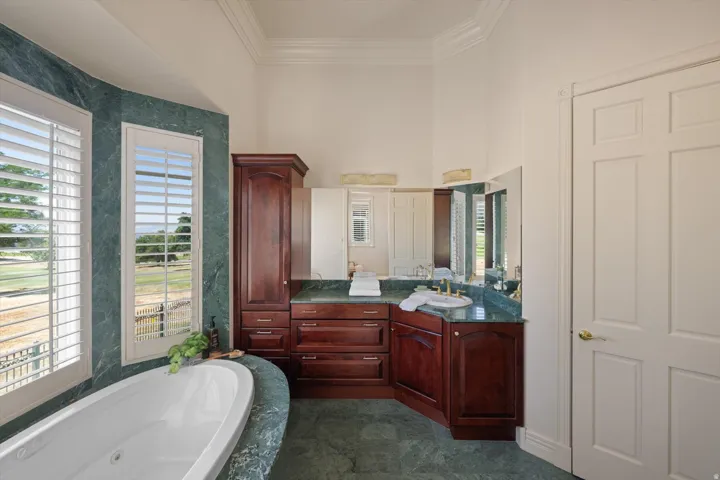 Bathroom featuring a freestanding soaking tub, expansive vanity with integrated sink, richly stained cabinetry, and large windows with plantation shutters