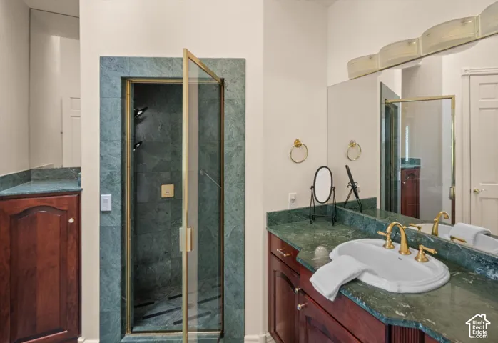 Bathroom featuring a glass-enclosed shower with gold-tone fixtures, a vanity with a green stone countertop, and wood cabinetry