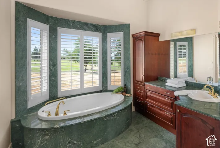 Soaking tub set in a green stone surround with brass fixtures and plantation shutters