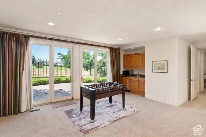 Room featuring glass patio doors in a walk out basement leading to Bonneville Golf Course, a built-in wet bar with wood cabinetry, recessed lighting, and crown molding