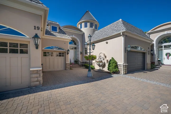 Paver driveway leading to a multi-car garage with arched windows and decorative outdoor lighting