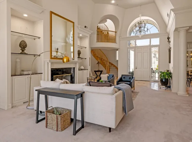 Spacious living area featuring a fireplace with a white mantel, built-in shelving with glass inserts, and high ceilings