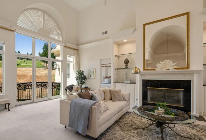 Living space featuring a tall ceiling, a large arched window, and French doors opening to a balcony with an ornate iron railing