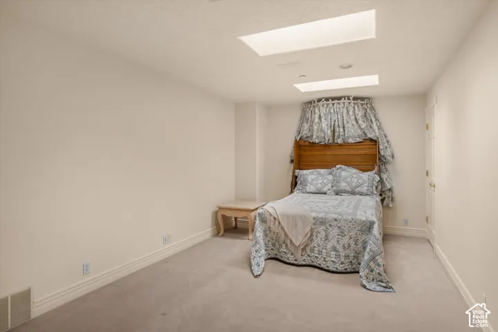 Recessed lighting and ceiling skylights illuminate a room featuring soft carpeting and white baseboards