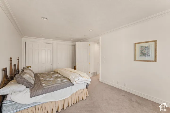 Carpeted bedroom featuring white walls, crown molding, recessed lighting, and white bi-fold closet doors