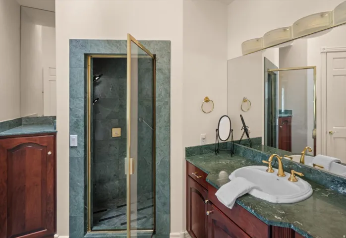 Bathroom featuring a glass-enclosed shower with gold-tone fixtures, a vanity with a green stone countertop, and wood cabinetry