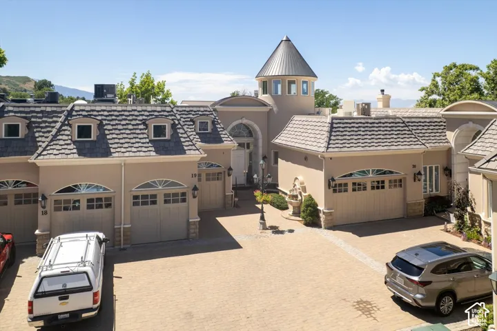 Stucco exterior featuring multiple garage doors with arched transom windows, a distinctive turret, and a paver driveway