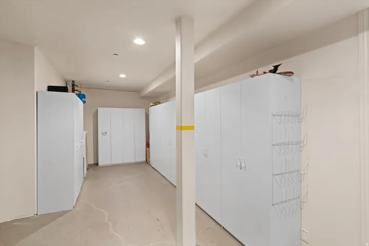 Dedicated storage area featuring multiple white cabinetry units, recessed ceiling lighting, a structural support column, light-toned walls, and concrete flooring