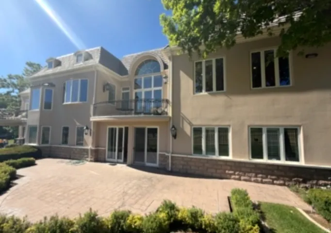 Spacious rear exterior featuring a multi-level stucco facade with stone detailing, a stamped concrete patio, and a second-story balcony with an ornate iron railing