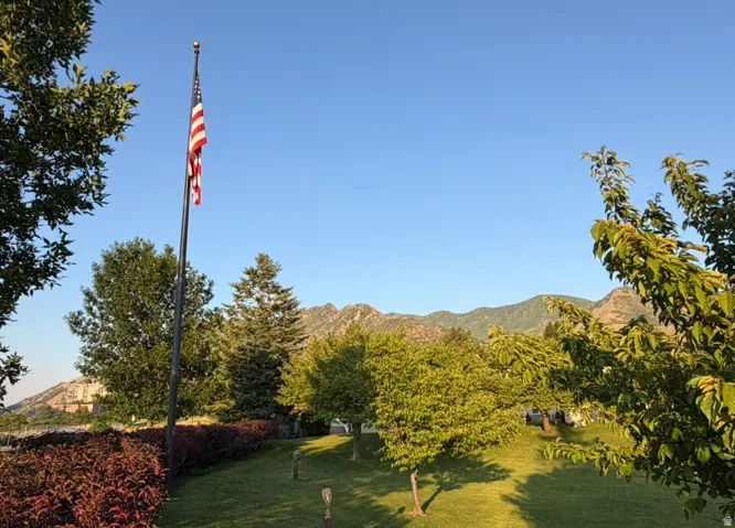 Expansive landscaped yard featuring a flagpole, mature trees, manicured lawn, and distant mountains