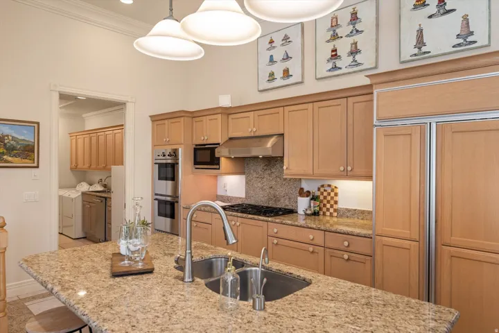 Gourmet kitchen featuring a large island with an undermount sink, granite countertops, wood cabinetry, stainless steel appliances, and high ceilings