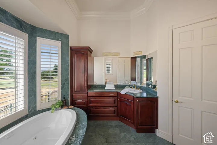 Bathroom featuring a freestanding soaking tub, expansive vanity with integrated sink, richly stained cabinetry, and large windows with plantation shutters