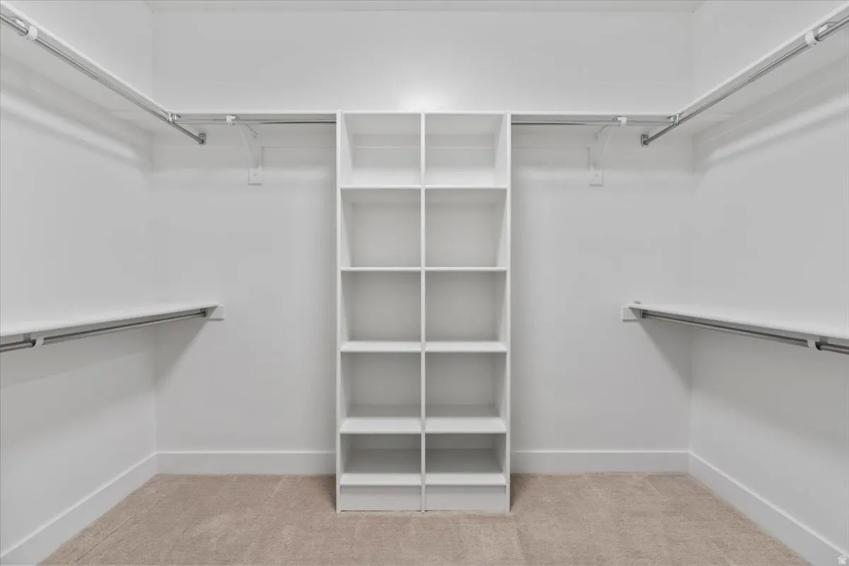 Walk-in closet featuring a central shelving unit with ten open compartments, dual-level hanging rods, wall-mounted shelving, and neutral carpet flooring