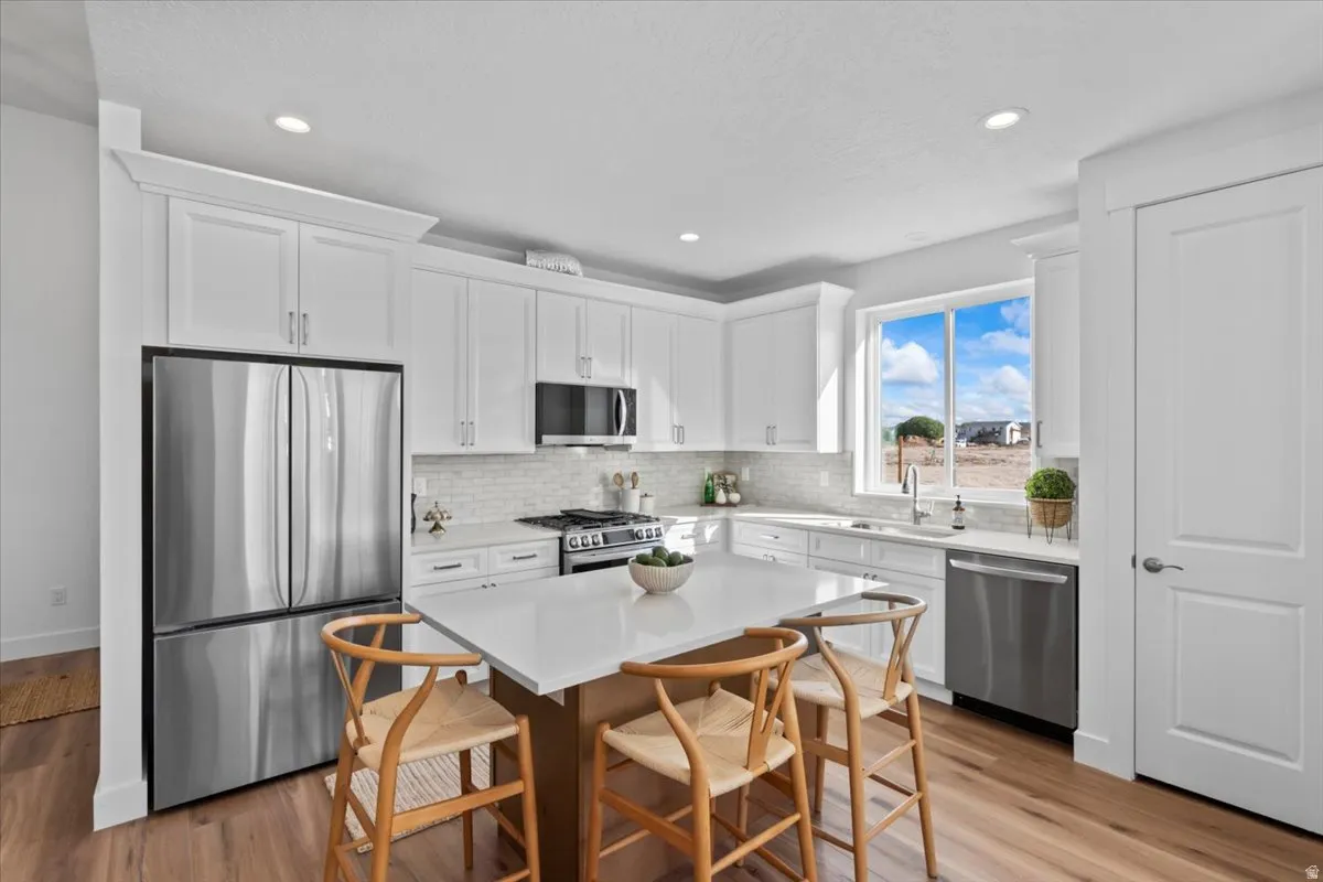 Modern kitchen featuring white cabinetry, stainless steel appliances, a center island with countertop seating, wood-finish flooring, and a subway tile backsplash