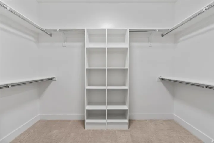 Walk-in closet featuring a central shelving unit with ten open compartments, dual-level hanging rods, wall-mounted shelving, and neutral carpet flooring