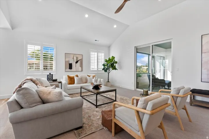 Spacious living area featuring a vaulted ceiling with a ceiling fan, recessed lighting, and large windows with plantation shutters