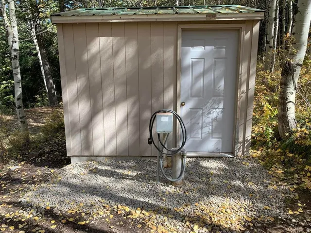 Storage shed featuring vertical panel siding, a white entry door, and a corrugated green metal roof