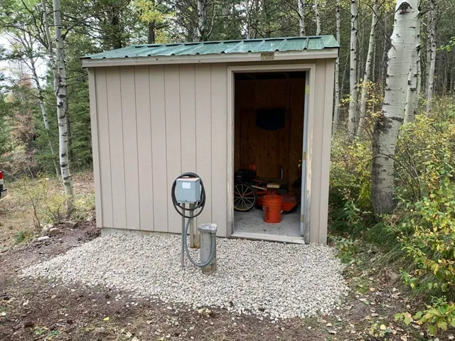 Utility shed with a green metal roof, light-colored siding, and a gravel base