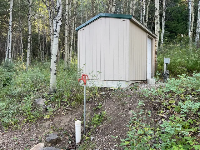 Utility shed with board and batten siding, a dark green roof, and a white access door