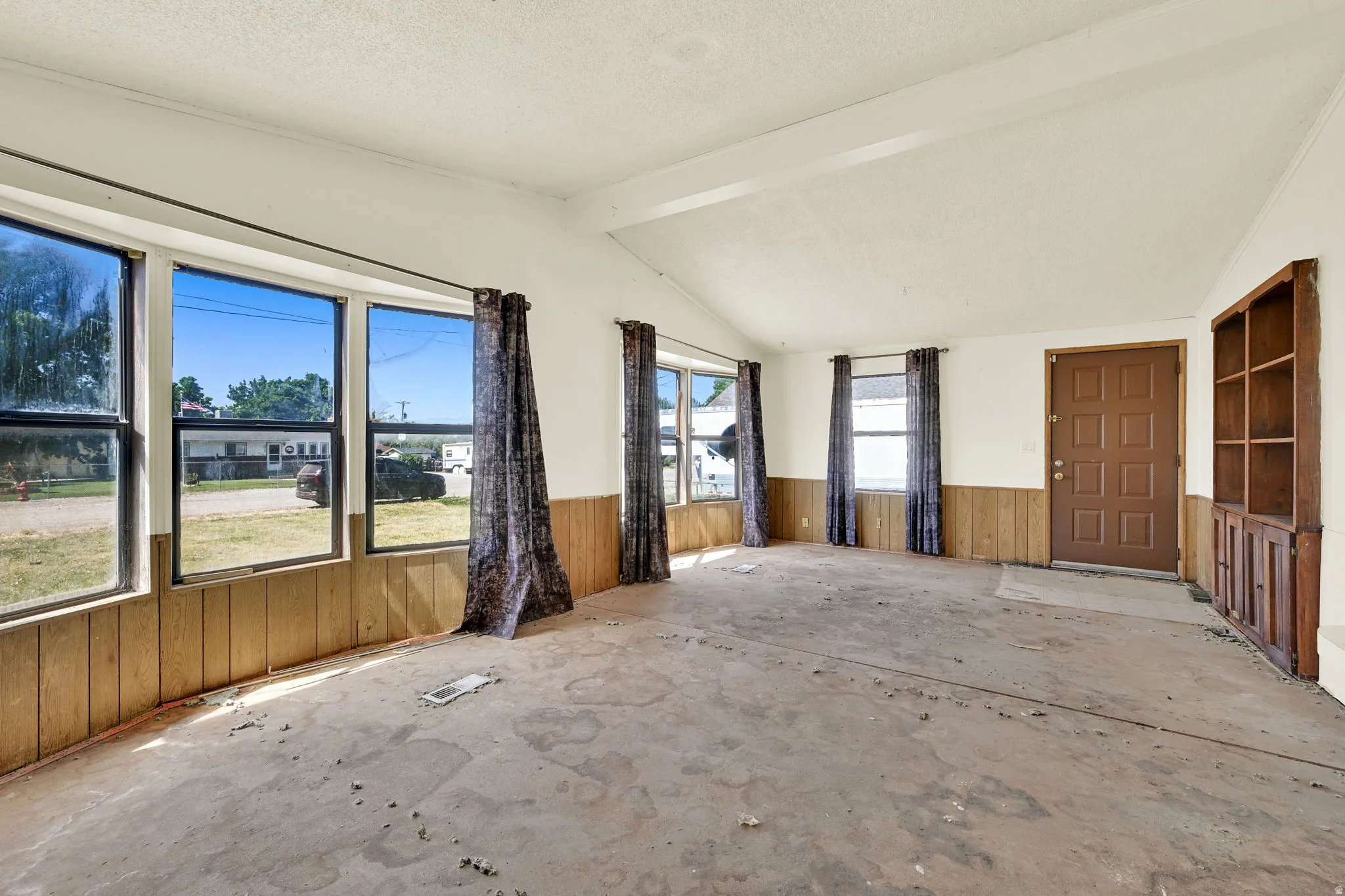 Spacious room featuring multiple large windows, wood paneling accents, a built-in wood shelving unit, and a paneled entry door