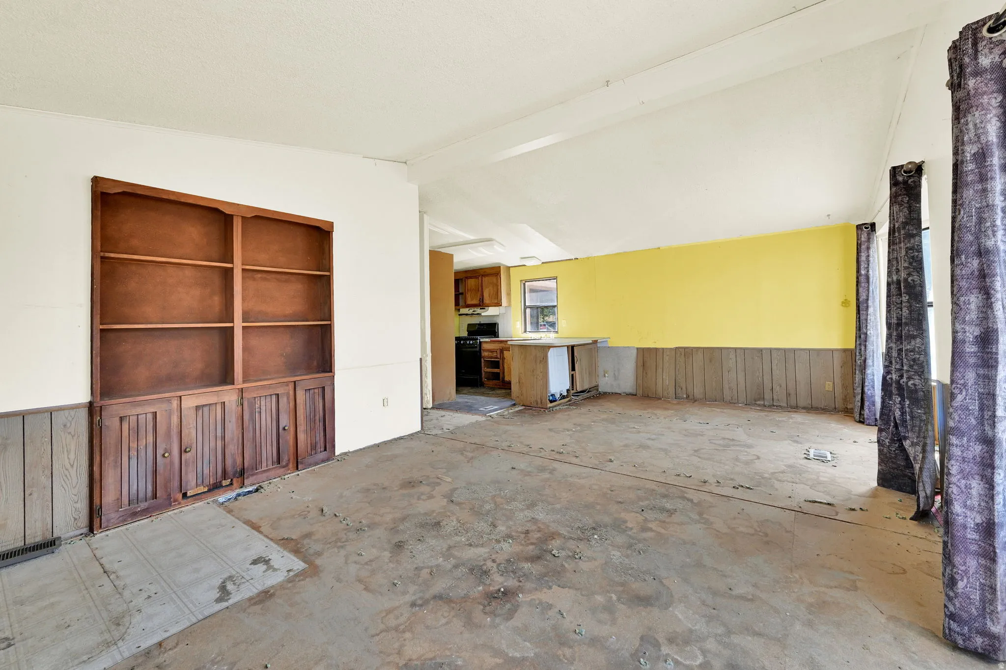 Open concept living area featuring a built-in wooden shelving unit, wainscoting paneling, and an exposed subfloor