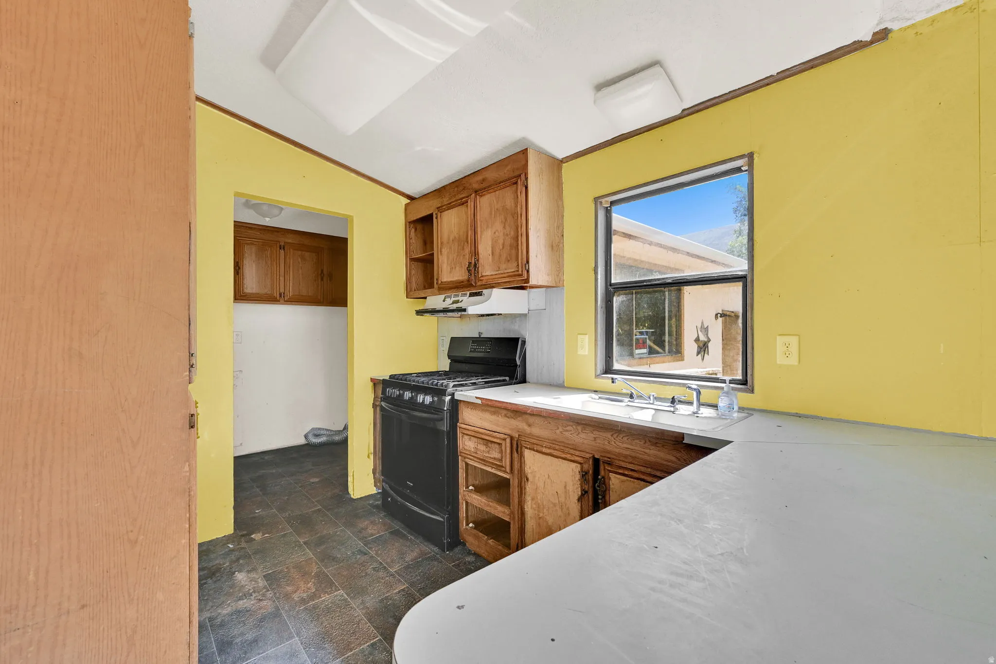 Kitchen featuring wood cabinetry, a black gas range with overhead exhaust, a stainless steel sink, and a window with exterior views