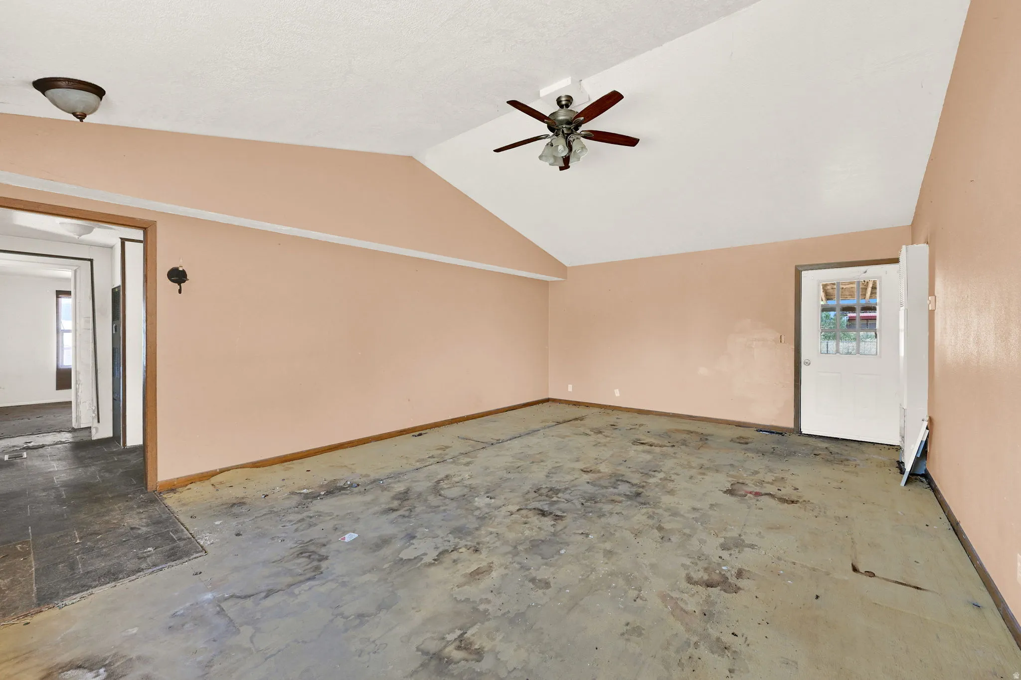 Interior space featuring a vaulted ceiling with a ceiling fan, a white exterior door with glass panels, and an interior doorway leading to an additional area