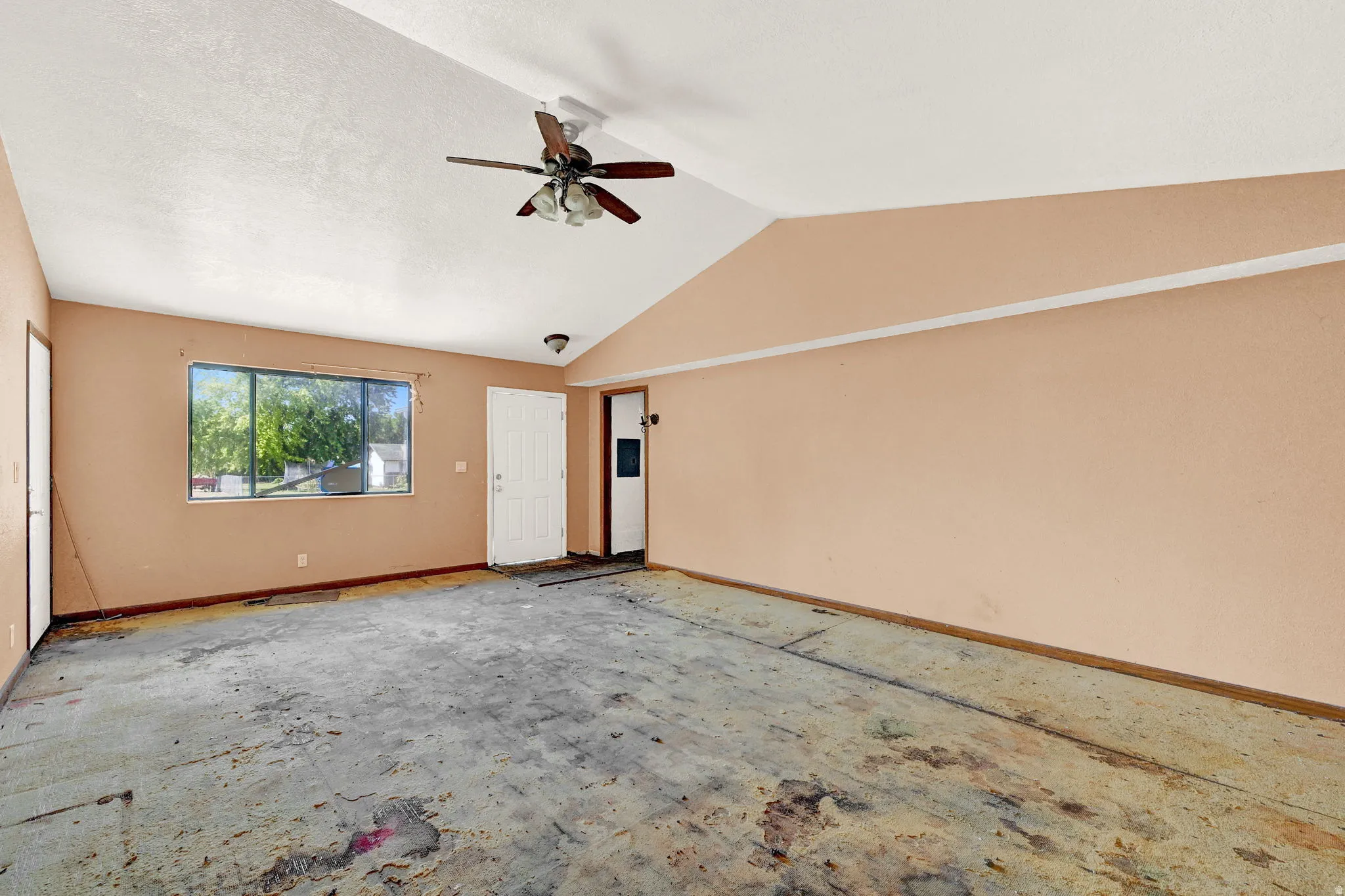 Spacious room featuring vaulted ceilings, a ceiling fan with integrated lighting, and a large window
